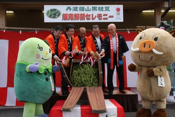 法被を着た市長と男性キャラクターのまるいのとまめりんが枝豆が入った樽をたたき、鏡開きをしている写真