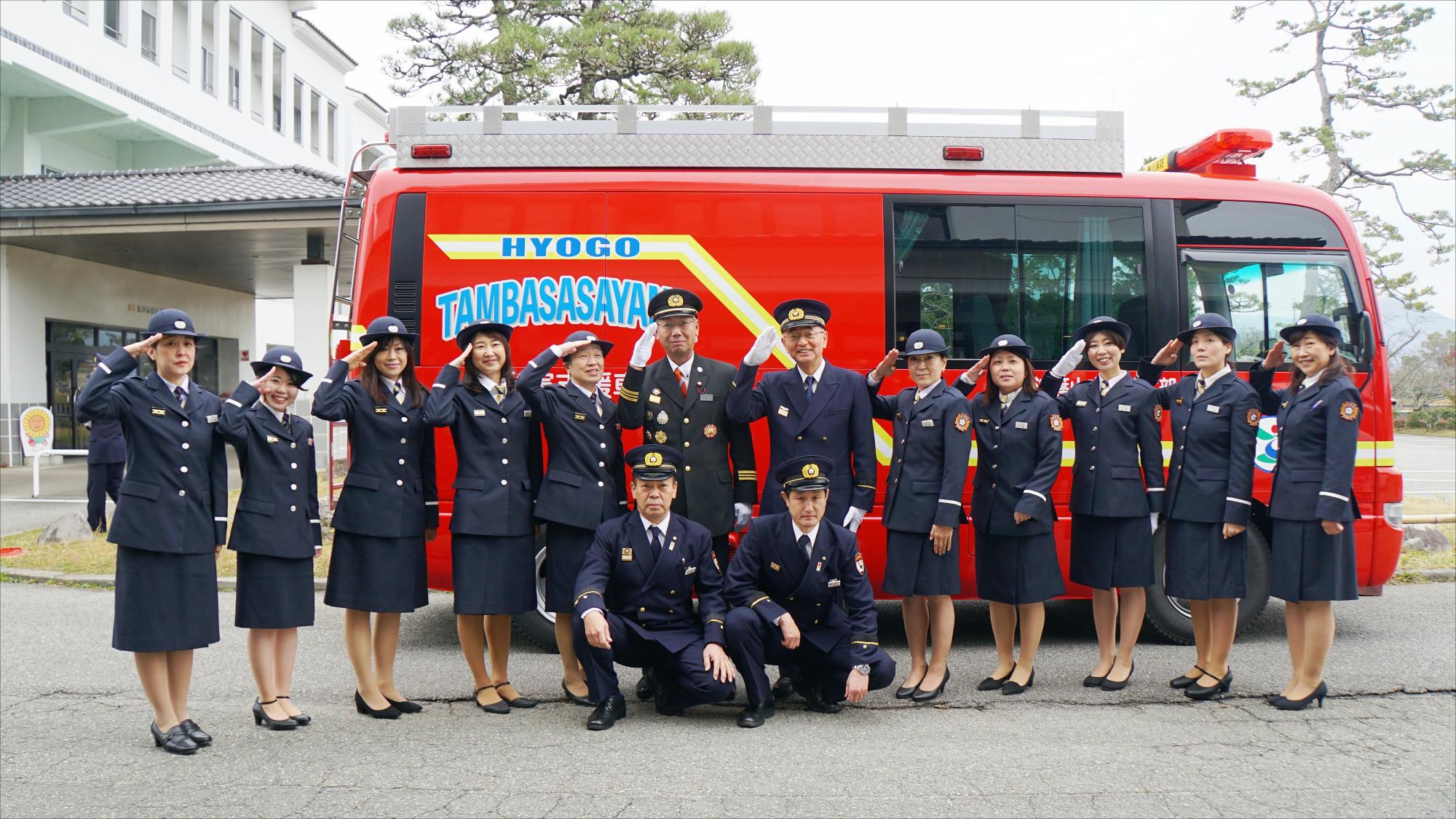 消防車の前で女性消防団員の方たちと市長などが敬礼している写真