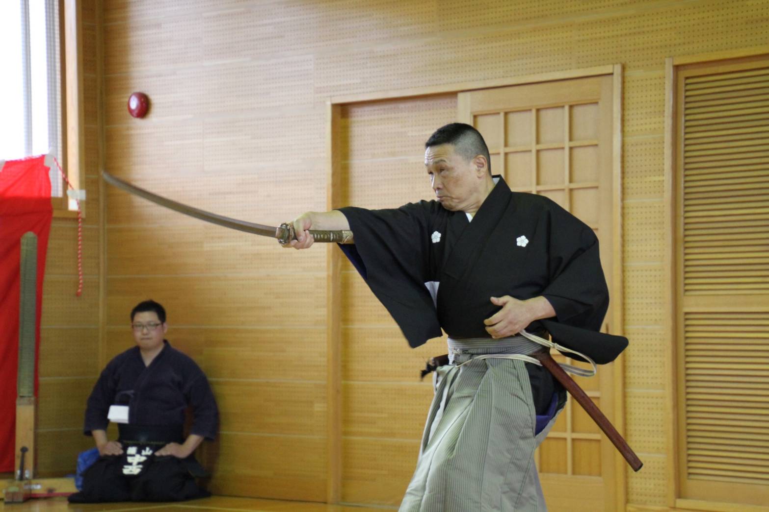 黒い袴を着た男性が、右手に持った剣を前に突き出している写真