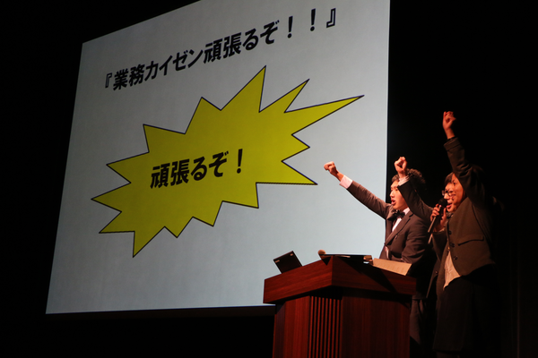 企画課がスクリーンに「業務カイゼン頑張るぞ！！」と掲げている写真