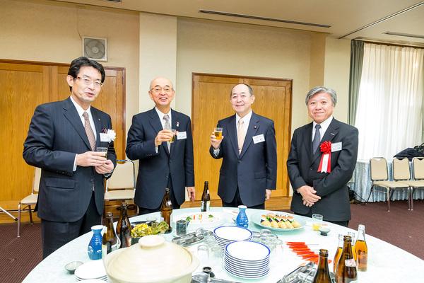 テーブルに料理やアルコールが置いてあり、高士社長、市長、足立議員がグラスを持っている写真