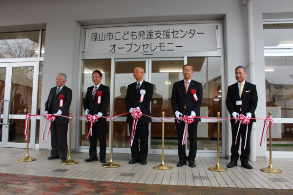 こども発達支援センター開所式のオープンセレモニーでテープカットをするスーツを着た男性5人の写真