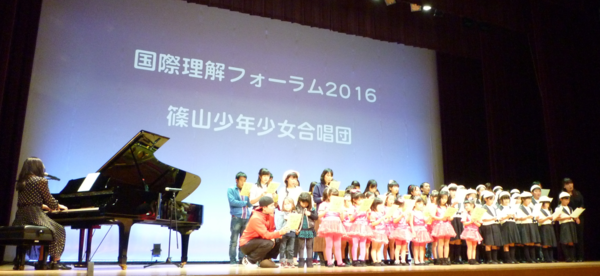 遠山 恵さんがピアノ伴奏しながら歌い、篠山少年少女合唱団の子供たちと合唱コラボしている写真