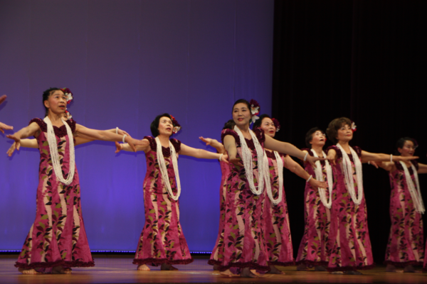 頭に花をつけて、お揃いのドレスを着て踊る女性たちの写真