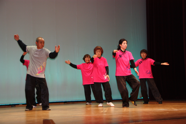 舞台で、ピンク色のシャツを着て踊る女性と男性の写真