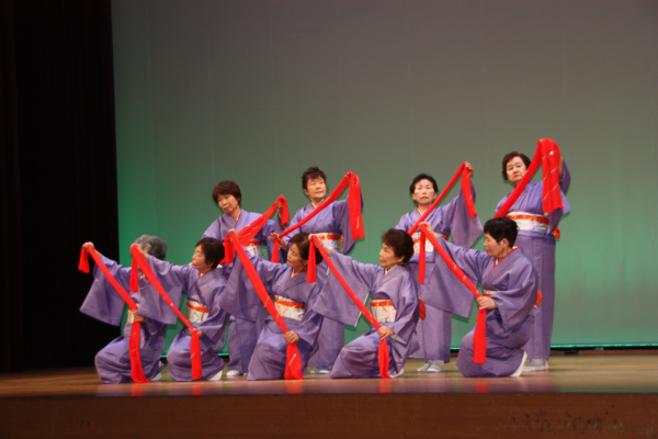 紫の浴衣を着て、手に赤い布をもってポーズをとる女性達の写真