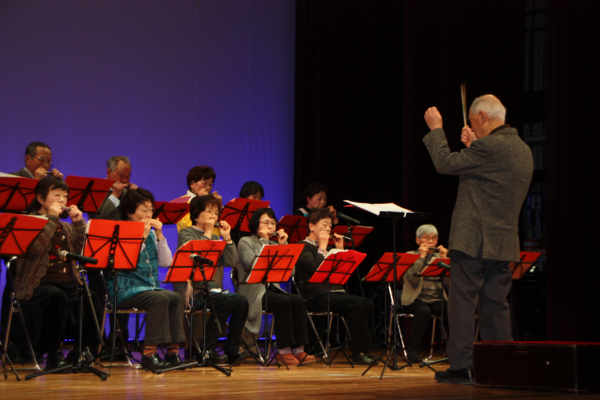 指揮者を見ながら演奏する男女の写真