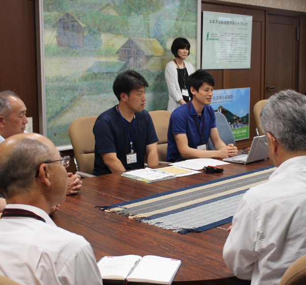 市長室にて、伊藤さんがパソコンを広げて、山本さんと活動報告をしている様子の写真