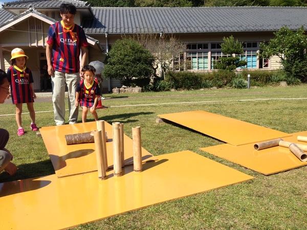 男の子が竹筒ボーリングをしているところをお姉ちゃんとお父さんが見守っている写真