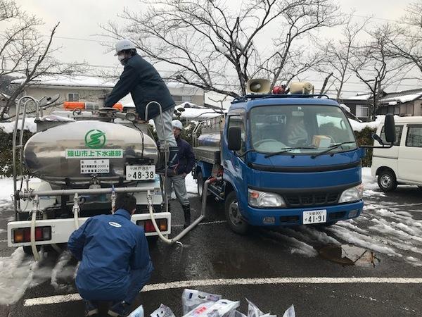 給水車が停車させている駐車場にも少し雪が積もりその中を職員の方が給水袋に水を入れている写真