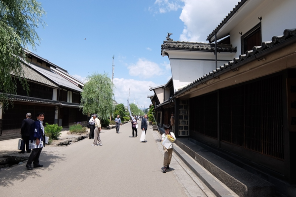 両脇に日本家屋が並ぶ道路を子供や男性達が歩いている写真