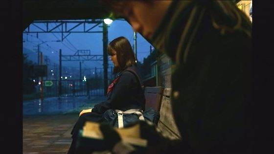 薄暗いなか、駅のプラットフォームの椅子に座って電車をまつ男女の学生の写真