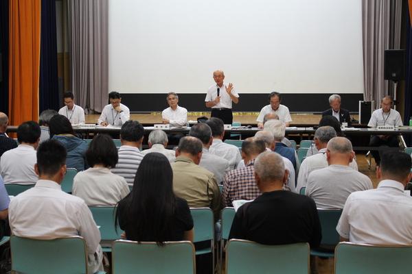 参加された方々が正面を向き、正面には市長やその関係者の方が座っており、市長がマイクを持って立ち、意見を述べている写真