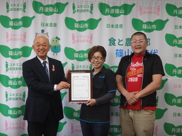 市長と呉田さん奥様が賞状を持ち、横に夫の哲一さん3人で記念写真