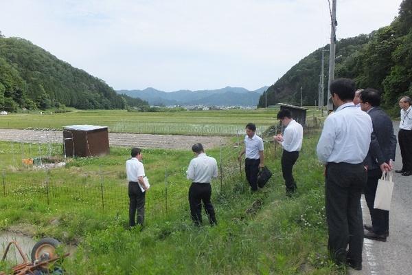 田んぼに設置されているサル用電気柵の現場を視察者へ説明している写真