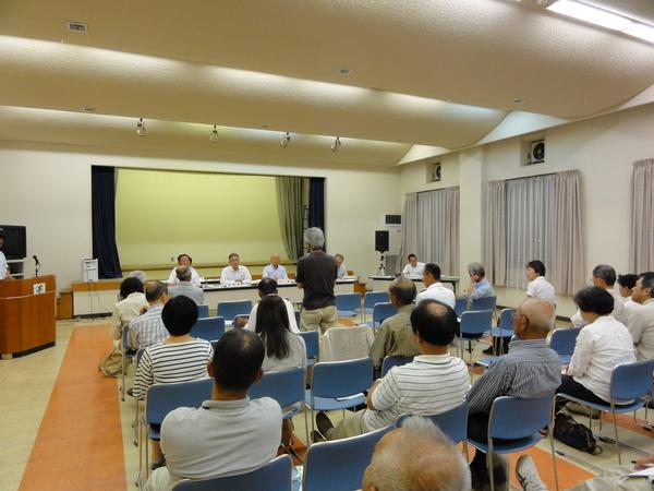 参加者の方々が、市長とその関係者と向かい合って座っており、1人の男性が立ち意見を述べている様子を後ろから写した写真