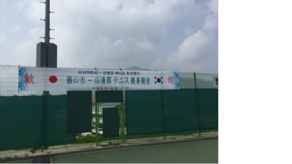 テニスコートの壁に貼られている、「歓迎 篠山市-山清郡テニス親善競技」と書かれている横断幕の写真