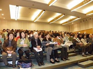 資料を手に着席している多くの聴衆者の写真