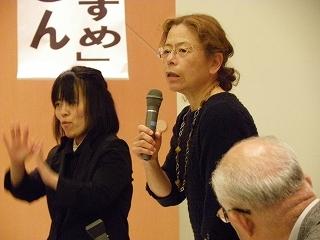 マイクをもって話をする高村 薫さんとその横で、手話をしている女性の写真