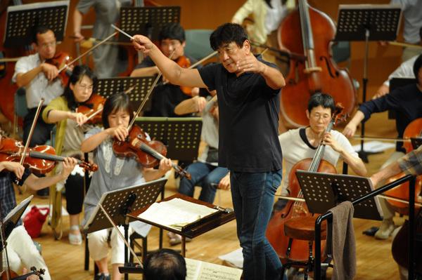 舞台でTシャツ姿の指揮者と演奏者が演奏している写真