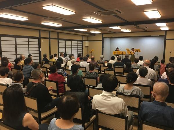 施設で2名の女性がバイオリンの演奏しているのを鑑賞している人々の写真