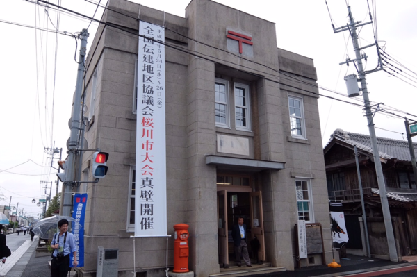 「全国伝建地区協議会桜川市大会真壁開催」とたたれた垂れ幕が飾られた郵便局の入口からの全体外観写真