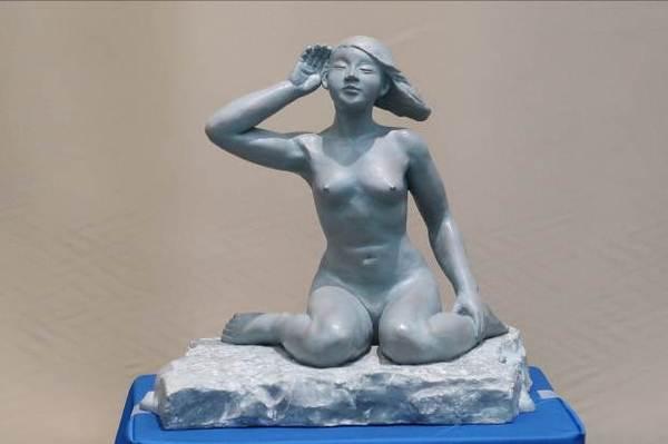 全裸の女性がべたん座りをして、右手を耳に当て風の音を聞いているような彫刻工芸の作品の写真