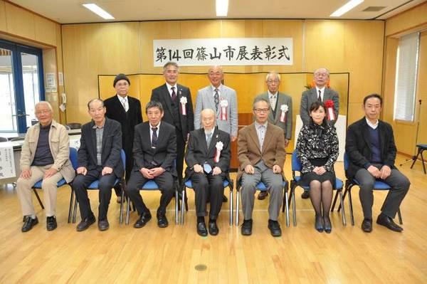 第14回篠山市展表彰式の横断幕の前で、受賞者が並んで座っており、2列目の中央に市長が立っている集合写真