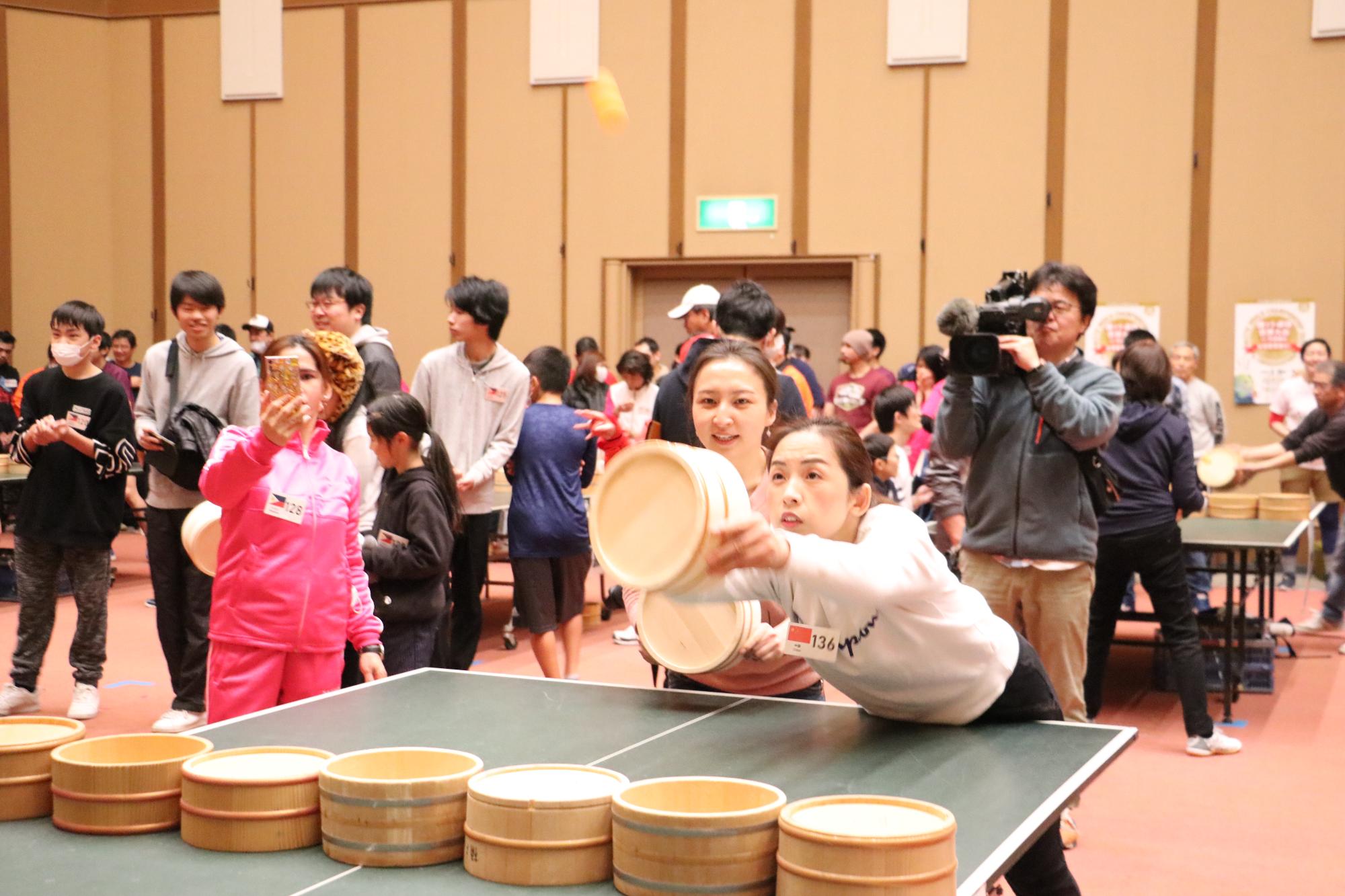 中国出身の女性のペアのうちの1人が、大きく体を前にして桶を突き出し、ピンポン玉を打った写真