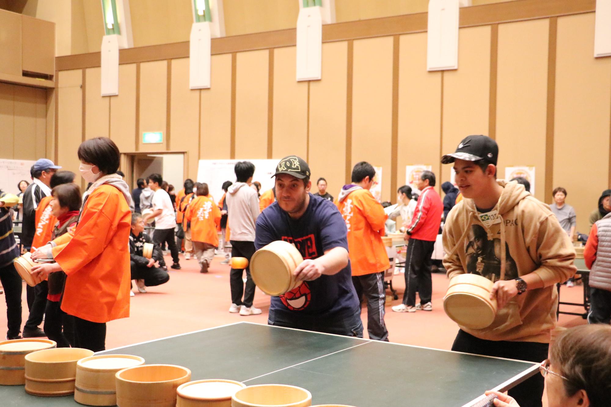 ブラジル出身の2人の男性のペアが試合をしており、紺色のTシャツを着た男性がピンポン玉を打ち返している写真
