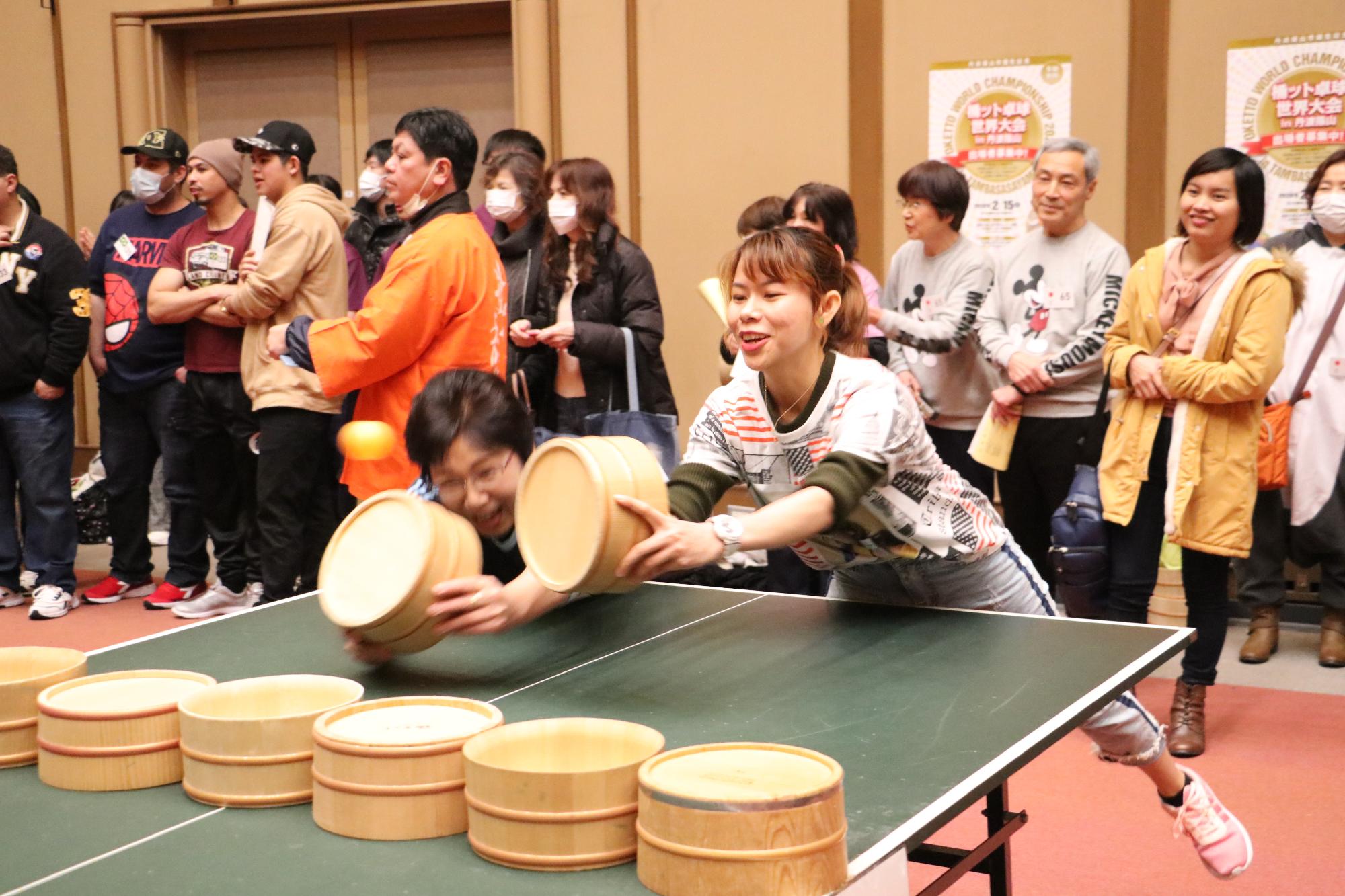 女性のペアが、体を大きく前にして必死にピンポン玉を返している写真