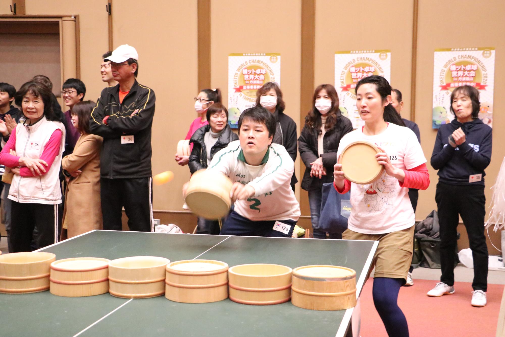 白い服を着た韓国出身の選手が2人、試合をしており、ピンポン玉をうった写真