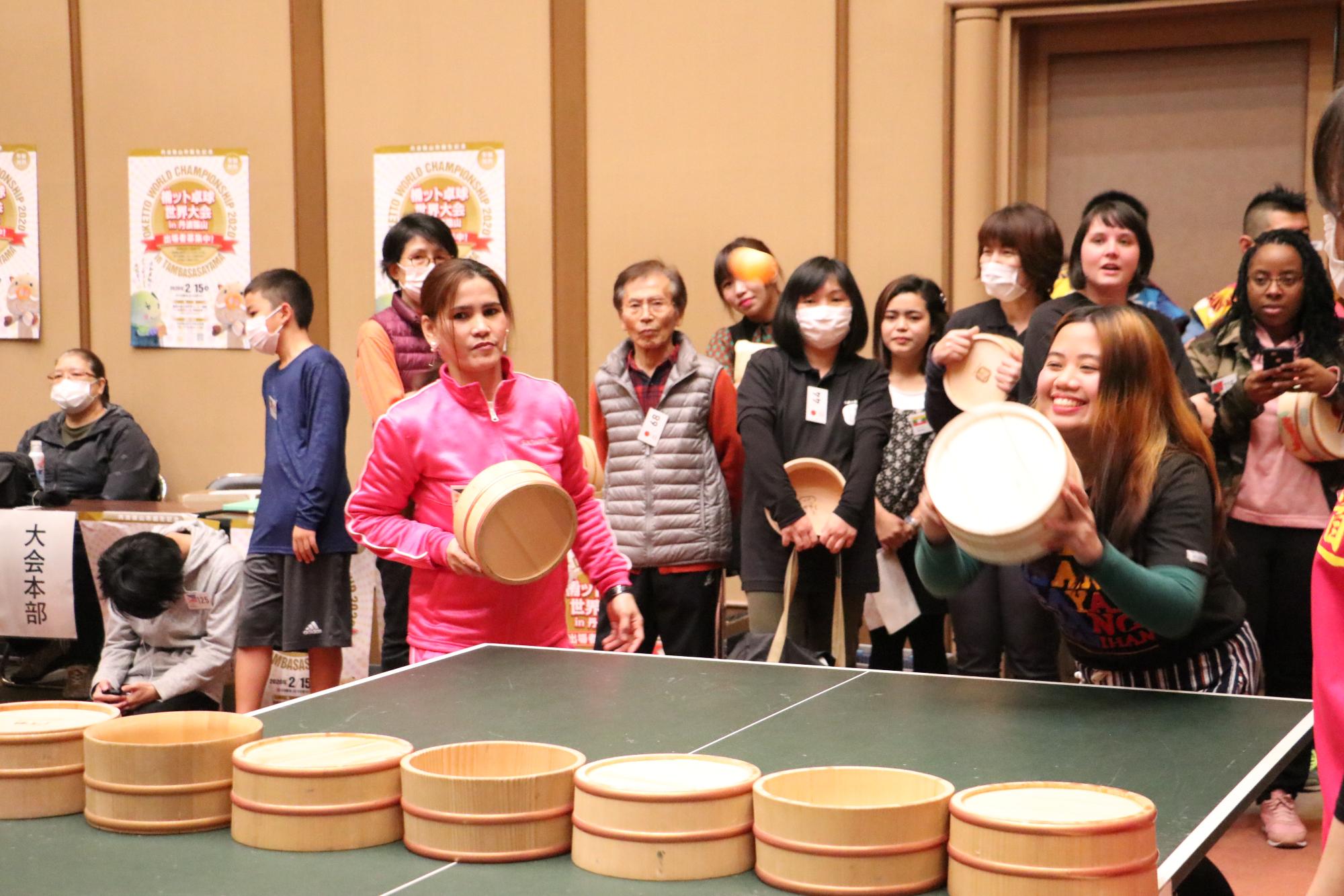 ピンクの服を着た女性が桶を持っており、笑顔の黒い服を着た女性が桶を構えている写真