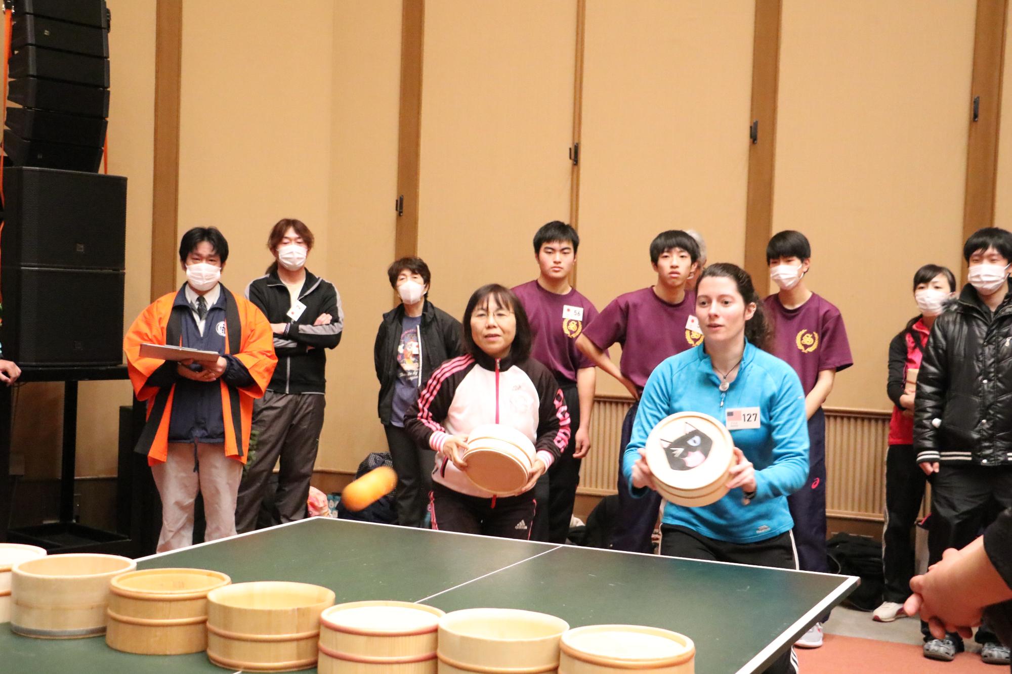 黒い猫のような動物が裏に描かれた桶を持ったアメリカ出身の女性と、白と黒の服を着た女性がペアになって試合をしている写真