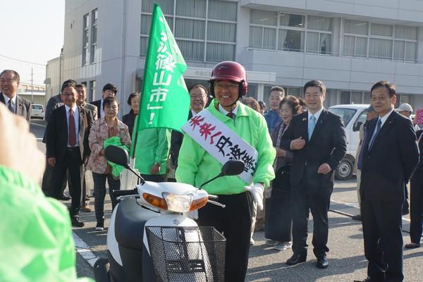 黄緑のジャンパーに黄緑の旗を立てスクーターで選挙活動へ行く前の市長の写真