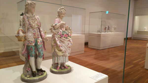 ショーガラスの中の、花がふんだんに描かれたドレスとスーツを着ている人形の置物の写真
