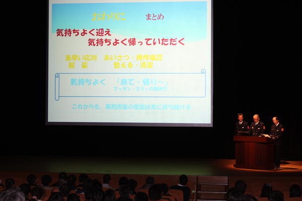 消防本部の発表で消防関係者が3名で壇上に立ちスクリーンで説明している写真