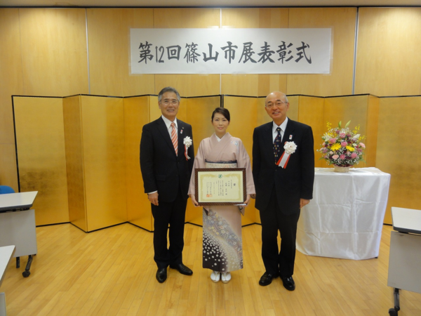 賞状を持った辻岡さん、市長、スーツ姿の男性が並んでいる写真