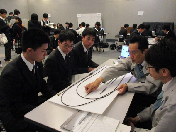 企業の方2名で男子生徒3人に模型を使って説明している写真