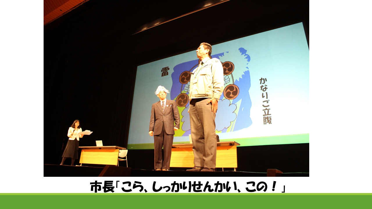 市長のお天気予報の雷のイラストがスライドに映し出され、職員と、その職員に雷さんをしようとする酒井市長の写真