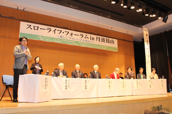 舞台の上に白いレースがかけられた長机にスーツを着た方達が座っている写真