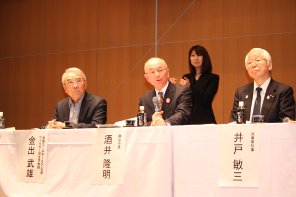 市長がマイクを持ってお話ししている後ろで女性が立って手話をしている写真