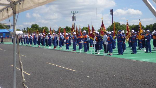 兵庫県広域防災センターで、青いユニフォームを着た沢山の消防団が、プラカードと旗をもち、整列している写真