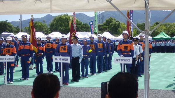 テントの中から見える、整列する消防団の写真