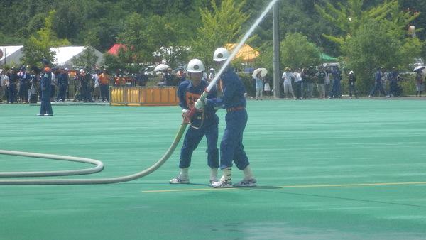 2人の団員が、一緒にホースを持ち、放水している写真