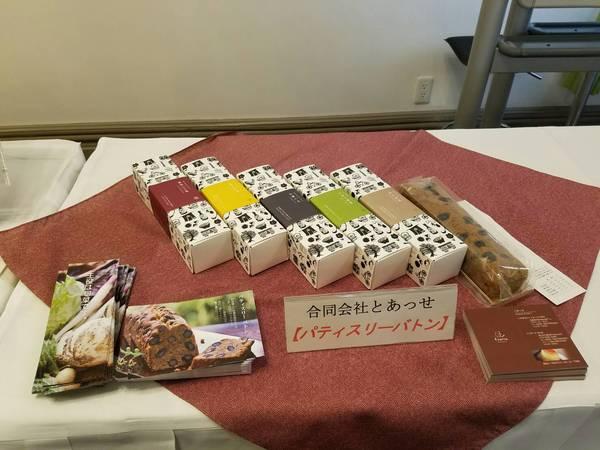 箱詰めされたパウンドケーキ5箱と黒大豆入りの袋詰めされたパウンドケーキとパンフレットがテーブルに展示されている写真