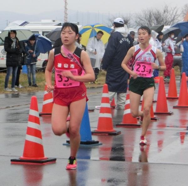 雨の中、傘をさす観客が見守る中、福佐さんが、後ろから迫りくる選手を前に必死に走っている写真