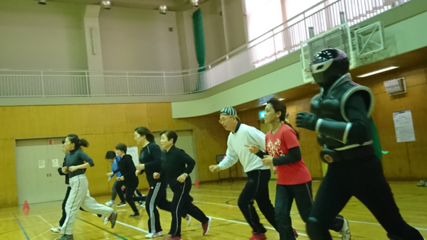 体育館にて、走り出している市長とご当地ヒーローササグロと複数の女性の写真