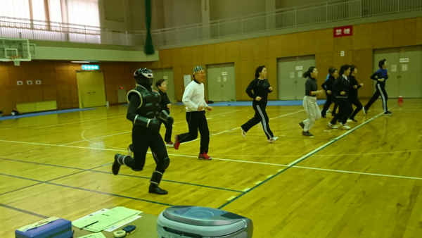 体育館で体力テストに参加している市長と参加者とニューヒーロー「ササグロー」が横一列に並んで走っている様子の写真