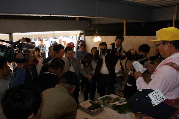 中央には箱に入った松茸が置かれその周りに人が集まり写真を撮ったり松茸を眺めている写真